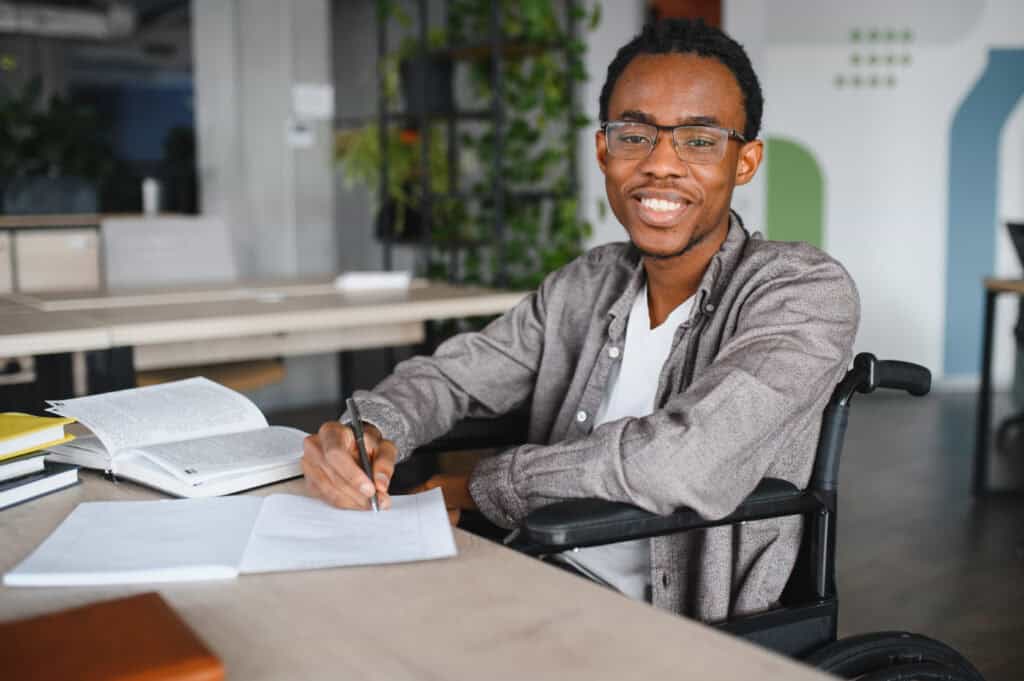 Smiling student in a wheelchair writing notes at a desk